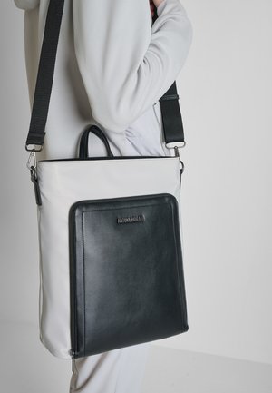 Persona con chaqueta blanca sosteniendo un bolso de hombro Antony Morato blanco y negro con correa ajustable negra.
