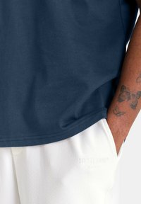 Camiseta de algodón azul marino de manga corta, con un cuello redondo. Combinada con pantalones blancos texturizados, que exhiben un logo de marca discreto.