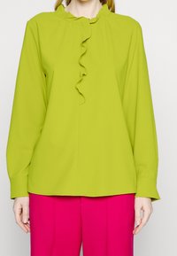 Lys grøn langærmet bluse med flæsekrave og glat stof. Sammen med livligt pink, brede bukser.