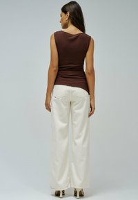Top sans manches côtelé marron associé à un pantalon large blanc, avec des poches arrière et une texture lisse sur un fond neutre.