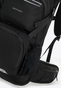 Mochila negra con un exterior texturizado, múltiples compartimentos, un bolsillo lateral de malla y correas ajustables. La marca es visible en la parte frontal.