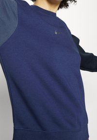 Marinblå sweatshirt med rund halsringning, långa ärmar och kontrasterande mörkare ärmar. Inkluderar en liten, metallisk Nike-logotyp på bröstet.