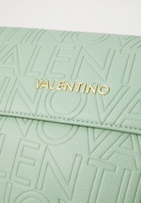 Borsa in pelle testurizzata verde menta con logo "Valentino" impresso e hardware dorato. Superficie liscia con motivo di caratteri pronunciati.