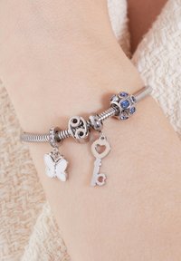 Zilveren armband met bedels in de vorm van een vlinder, een hartvormige sleutel en blauwe stenen accenten; soepel, flexibel band met een gestructureerd ontwerp.