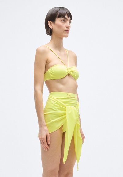 Világos sárga bikini felső csavart elülső résszel; hozzáillő, deréknál csomós részletű wrap szoknyával párosítva. Simogató, rugalmas anyag.