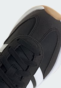 Čierna športová obuv s textúrovaným textilným zvrškom, sieťovanými akcentmi, čiernymi šnúrkami, bielymi pruhmi a gumovou podrážkou s béžovým špičkou.