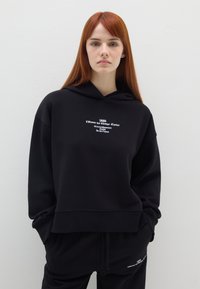 Zwarte hoodie van een katoenmengsel, met een ontspannen pasvorm, een kangoeroezak en witte tekstafbeeldingen op de voorkant en onderzoom.