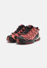 Chaussures de trail running avec un design rouge et noir, présentant une tige en mesh, une semelle texturée et un système de laçage sécurisé. Matériau Gore-Tex inclus.