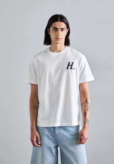 Valge puuvillane T-särk lühikeste varrukatega, mille vasakul rinnal on must "HL" logo; sobitatud helesiniste denimpükstega.