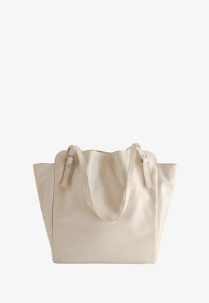 Beige leren shopper met gekartelde bovenranden, twee verstelbare schouderbanden met zilveren gespen en een licht slungelige vorm.