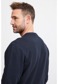 Felpa blu navy con colletto tondo, cuciture visibili e una texture morbida. La vista posteriore mette in evidenza il suo design casual e la forma aderente.