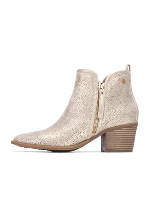 Botines beige con superficie texturizada, tacón alto, cremallera lateral y un patrón sutil de pequeños perforados. Diseño de punta redondeada.