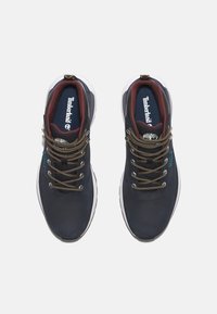 Zapatillas de cuero azul oscuro con un acabado texturizado, con detalles en marrón, cordones dorados y una suela de goma blanca. Logo de Timberland visible.