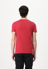 Rotes Kurzarm-T-Shirt aus weichem, strukturiertem Stoff. Standard Rundhalsausschnitt und gerader Saum, getragen mit dunklen Jeans, von hinten betrachtet.