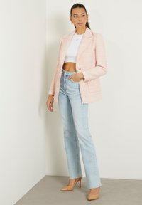 Blazer di tweed rosa chiaro con due tasche frontali e bottoni dorati, abbinato a jeans dritti azzurri e décolleté color nude.