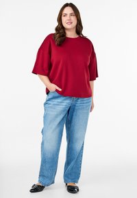 Červená oversized mikina s krátkym rukávom a okrúhlym výstrihom, v kombinácii s svetlomodrými voľnými džínsy a čiernymi balerínkami. Neformálny outfit.