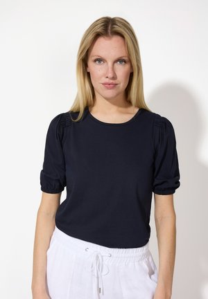 Haut bleu marine à manches courtes avec des manches bouffantes froncées, un col ras du cou et un tissu doux, associé à un pantalon blanc à cordon de serrage.