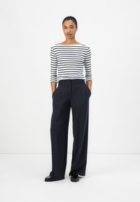 Gestreiftes Langarmoberteil in Weiß und Marineblau, kombiniert mit hochtaillierten, weit geschnittenen Marineblauen Hosen. Schwarze Schuhe mit Struktur- und Designdetails.