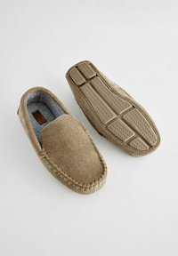 Mocassins en tissu marron avec un extérieur texturé, une doublure grise douce et une semelle en caoutchouc présentant un motif en zigzag pour l'adhérence.