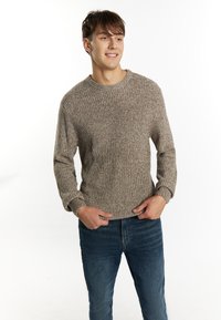Pulover tricotat cu un model bej și maro melanj, decolteu rotund, textură ribbed și mâneci lungi. Asortat cu blugi din denim albastru.