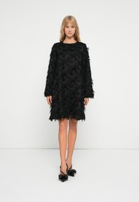 Μαύρο φόρεμα με μακριά μανίκια, υφή λουλουδιών και λεπτομέρειες με κρόσσια. Συνδυασμένο με μαύρες μυτερές γόβες με φιόγκους.