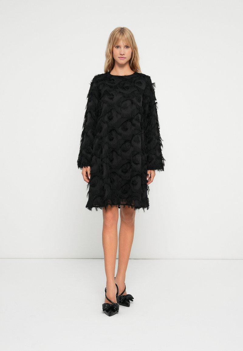 Μαύρο φόρεμα με μακριά μανίκια, υφή λουλουδιών και λεπτομέρειες με κρόσσια. Συνδυασμένο με μαύρες μυτερές γόβες με φιόγκους.