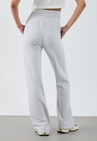 Hellgraue, weit geschnittene Sweatpants mit einem elastischen Bund und glatter Textur, die an den Hüften eng anliegen und an den Beinen ausgestellt sind.