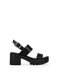 Sandalias de plataforma de cuero negro con un tacón robusto, correa en el tobillo ajustable y diseño cruzado en la parte superior. Suela texturizada para un mejor agarre.
