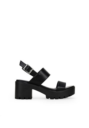Sandalias de plataforma de cuero negro con un tacón robusto, correa en el tobillo ajustable y diseño cruzado en la parte superior. Suela texturizada para un mejor agarre.
