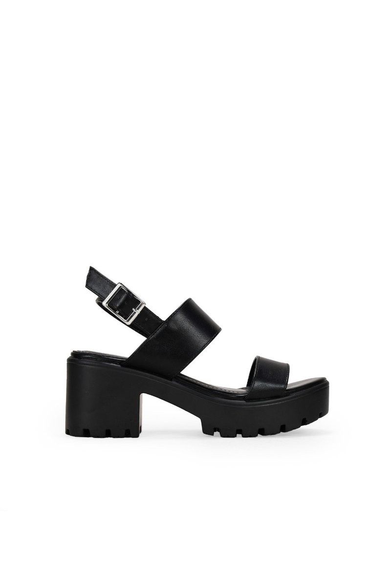 Sandalias de plataforma de cuero negro con un tacón robusto, correa en el tobillo ajustable y diseño cruzado en la parte superior. Suela texturizada para un mejor agarre.
