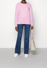 Sudadera de algodón rosa con detalles perforados en las mangas, combinada con jeans acampanados azules. Se incluyen zapatillas blancas y un bolso beige claro.