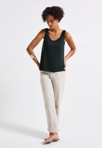 Musta hihaton paita leveillä ribbihihnoilla, yhdistettynä vaaleanbeigeihin suoriin housuihin ja litteisiin sandaaleihin, esiteltynä neutraalilla taustalla.