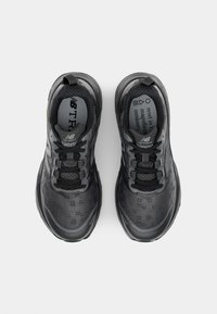 Zwarte sportschoenen met een gestructureerde bovenkant, veters, een gewatteerde kraag en een dikke rubberen zool met subtiele merktekens.