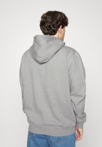 Sudadera con capucha gris de textura suave, ajuste casual y puños acanalados. La parte posterior presenta una gran capucha y un detalle mínimo.