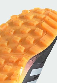 Suela de zapato deportivo negro con lengüetas de tracción de goma naranja, que presenta formas rectangulares y una superficie texturizada para agarre y estabilidad.