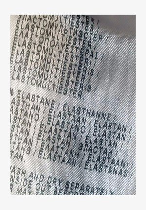 Návod na údržbu odevu uvádzajúci zloženie látky, prevažne polyester a elastan, v niekoľkých jazykoch na bielom textúrovanom materiáli.