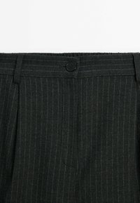 Pantalons à rayures gris foncé avec une taille plate, dotés d'un seul bouton noir, de plis et d'un tissu texturé subtil.