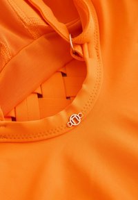 Close-up van een helder oranje stof met een gladde textuur, met een geweven patroon en een metalen lusaccent op de strap.