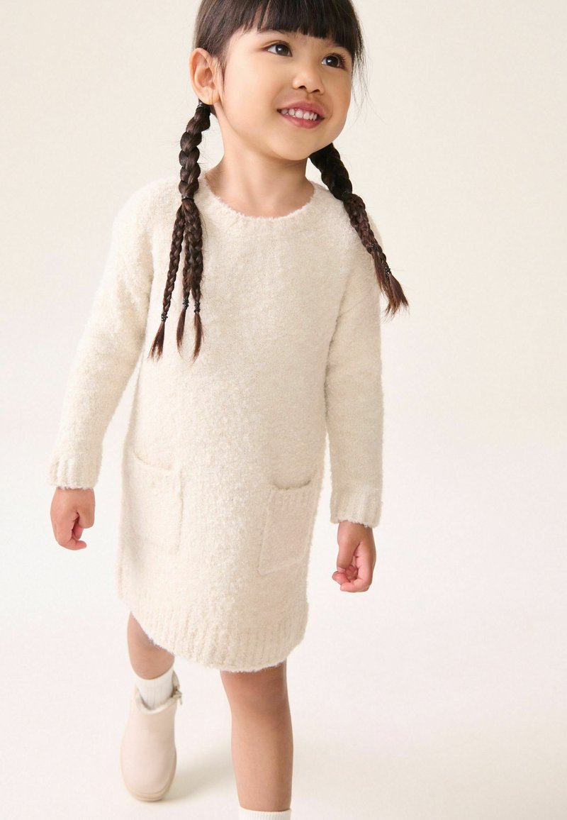 Robe crème à manches longues en matériau texturé duveteux, dotée de deux poches avant et de poignets côtelés, associée à des bottines légères à la cheville.