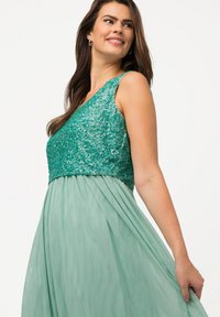 Vestido verde con parte superior de lentejuelas y escote en V, y una falda fluida y texturizada. El corsé está ajustado, mientras que la falda tiene un diseño aéreo y en capas.