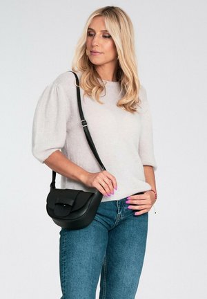 Jasnoszary sweter z krótkim rękawem i bufkami na ramionach; w połączeniu z ciemnoniebieskimi dżinsami. Czarna torebka na ramię z zaokrągloną klapką i regulowanym paskiem.