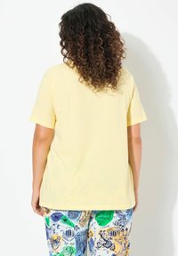 Žluté tričko s krátkým rukávem a volným střihem, spárované s vzorovanými pyžamovými kalhotami s různými barevnými ilustracemi.