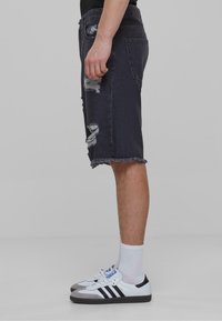 Pantalones cortos de mezclilla negra con detalles rasgados, dobladillo deshilachado y un diseño de cinco bolsillos. Combinados con zapatillas blancas y calcetines hasta el tobillo.
