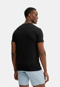 Maglietta nera a maniche corte con scollo rotondo, realizzata in tessuto misto cotone, design aderente con una texture liscia e stile minimalista.