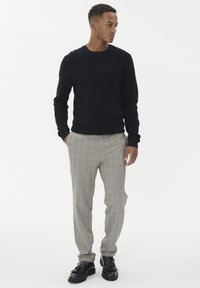 Czarny sweter dzianinowy, szare spodnie w kratę i czarne skórzane buty z chwostami. Spodnie mają subtelne żółte i niebieskie linie.