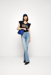 T-shirt nera con design a stampa leopardata e maniche a volant, jeans svasati blu chiaro, stivali neri con tacco e borsa blu.