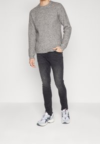 Suéter de punto acanalado gris con cuello redondo, combinado con jeans ajustados negros y zapatillas blancas con detalles en gris y negro.