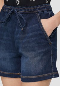 Ciemnoniebieskie szorty dżinsowe z elastycznym paskiem i sznurkiem. Posiadają dwie boczne kieszenie oraz kontrastowe przeszycia wzdłuż dołu.