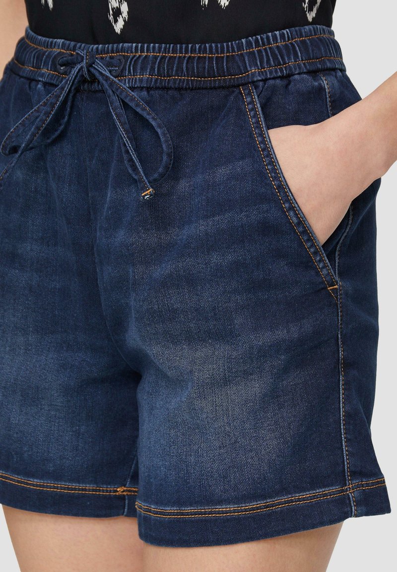 Ciemnoniebieskie szorty dżinsowe z elastycznym paskiem i sznurkiem. Posiadają dwie boczne kieszenie oraz kontrastowe przeszycia wzdłuż dołu.