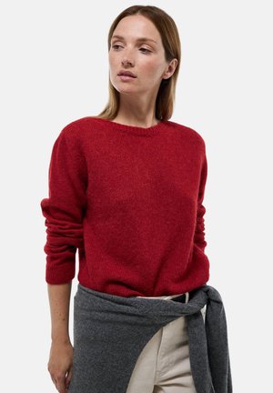 Sweater en tricot rouge avec un col rond et des manches longues, associé à un châle en tricot gris noué autour de la taille. Design simple, texture douce.